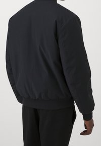 Svart bomberjacka med en slät utsida, ribbade ärmslut och nederkant, samt en avslappnad passform. Har en rund halsringning och ingen synlig hårdvara.