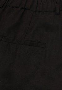 Svart tyg med en texturerad väv, med en elastisk midja och en liten fickdetalj på framsidan.