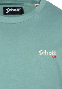 Lekka bawełniana koszulka w kolorze jasnozielonym z okrągłym dekoltem. Z przodu, po lewej stronie, znajduje się biało-czerwone haftowane logo "Schott N.Y.C.".