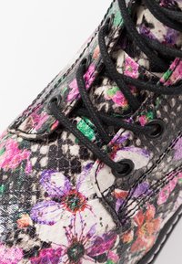 Bottes à lacets à imprimé floral avec un fond texturé noir et blanc, des fleurs colorées et des œillets ronds noirs pour les lacets.