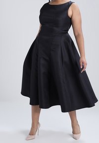 Svart ärmlös klänning med en figurnära bodice och utsvängd kjol, tillverkad av slät tyg. Har en båt-halsringning och sidofickor.