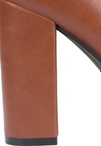 Brown textured high-heeled shoe with a chunky rectangular heel and black sole. The material appears leather-like, with visible grain pattern.