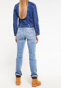 Džínová bunda v tmavě modré barvě, doplněná o světle modré džíny s prošitými zadními kapsami. Hnědé boty s gumovou podrážkou. Jednoduchý design.