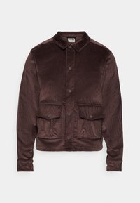 Brun kordjacka med krage, framknäppning och två bröstfickor. Strukturerad yta och kortad design.