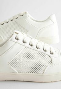 Białe skórzane sneakersy mają perforowane boki, płaskie sznurowadła i gumową podeszwę. Okrągły czubek i gładkie wykończenie z oczkowymi akcentami.