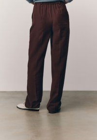 Pantaloni marroni ampi con vita elastica, tessuto liscio e tasche laterali; abbinati a mocassini bianchi.