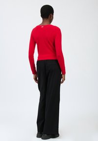 Maglione rosso a maniche lunghe con orlo a coste e texture liscia. Abbinato a pantaloni neri larghi e stivali neri robusti.