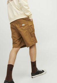 Shorts cargo maro cu multiple buzunare, din material textil din bumbac, cu croi drept. Purtați cu șosete închise la culoare și adidași negri.