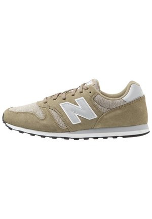 Chaussure de sport beige avec dessus en suède et mesh, accents blancs, fermeture à lacets, semelle extérieure en caoutchouc et logo blanc prominent sur le côté.