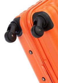 Valise rigide orange avec une surface texturée, dotée de roues noires et d'une fermeture éclair, mettant en avant sa construction durable.