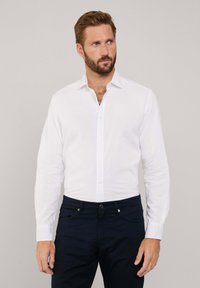 Witte dress shirt gemaakt van linnen, met een puntige kraag, knoopsluiting en lange mouwen. Gecombineerd met donkerblauwe broek.
