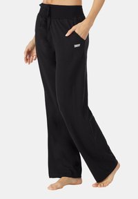 Zwarte loungebroek met een trekkoord in de taille, wijde pijpen en zijzakken. Heeft een witte "DKNY" logo op de rechter voorzak. Soepele textuur.