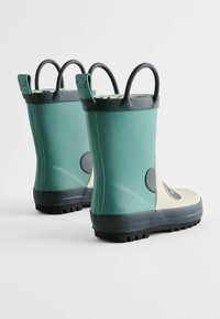 Bottes de pluie en caoutchouc teal et crème avec des semelles noires. Présentent une forme arrondie, des accentuations sur le thème des ours et deux poignées de transport.