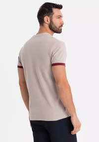 Beige kortærmet t-shirt med maroon ribbet krave. Har en rund halsudskæring, tætsiddende design og en glat bomuldsstruktur.
