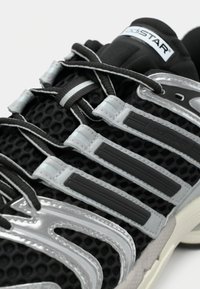 Must jooksujalanõu võrgumaterjalist, hõbedaste sünteetiliste detailide ja hallide paeltega. Omab kolme horisontaalset triipu ja tekstureeritud tallaga.