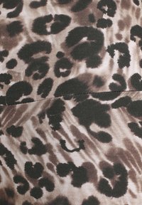 Leopardprint stof met een beige en bruine kleurenschema en onregelmatige zwarte vlekken. Getextureerd breimateriaal met een gladde afwerking.
