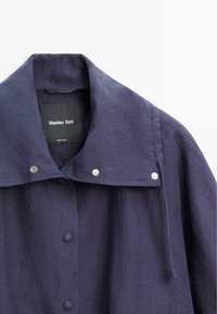 Granatowa kurtka zapinana na guziki z szerokim kołnierzem i trzema srebrnymi zatrzaskami na kołnierzu, z widoczną metką Massimo Dutti wewnątrz.