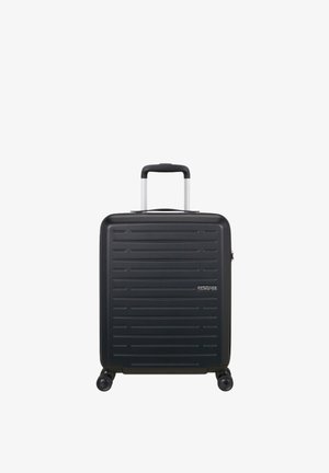 Valigia rigida nera con scanalature orizzontali, quattro ruote e manico telescopico esteso, con il marchio American Tourister sul lato frontale.