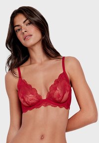 Brassière en dentelle rouge avec motif floral, bonnets transparents, bretelles ajustables et bandeau doux. Présente de délicats bords festonnés.