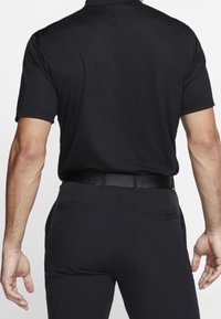 Black polo shirt with short sleeves, smooth texture, and a classic collar, paired with dark pants and a black belt, showcasing a simple design.