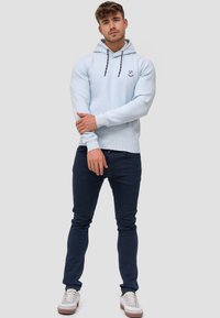 Světle modrá mikina s texturovaným povrchem, s logem na náprsní kapse a černými tkaničkami. Kombinováno s tmavě modrými slim-fit džíny a b�ílými teniskami.