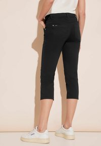 Černé krátké kalhoty s úzkým střihem, plochým pasem, dvěma zadními kapsami a hladkou, elastickou texturou. Doplněno bílými teniskami.