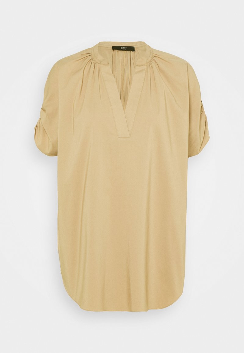 Blouse beige à manches courtes avec un col en V, épaules froncées et un petit col montant, présentée sur un fond uni.