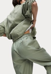 Overmaat groene jas en bijpassende elastische broek, gemaakt van zacht, textuurstof, met een achterzak op de broek.