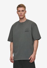 Mørk grå oversized t-shirt lavet af bomuld, med en rund halsudskæring og korte ærmer, samt et lille logo på brystet.