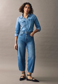 Jasnoniebieska denimowa koszula z kieszeniami i zapięciem na guziki, w połączeniu z niebieskimi dżinsami wysokiego stanu. Czarne baleriny z paskami na kostce i ćwiekami.