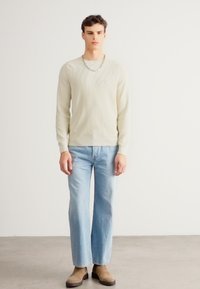 Svetločervený pletený sveter s rebrovaným lemom a výstrihom, nosený s svetlomodrými širokými džínsami a hnedými členkovými čižmami. Jednoduchý náhrdelník s reťazou.