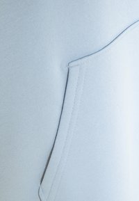 Tissu bleu clair en gros plan montrant une poche cousue avec des coutures nettes et un tissage finement texturé, conforme au coton ou à un matériau similaire.