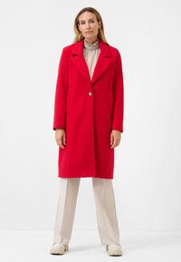 Rode wollen mix jas met een kraag, enkele knoopsluiting, twee voorzakken en lange mouwen. Draag over een licht gerimpeld blouse en beige broek.