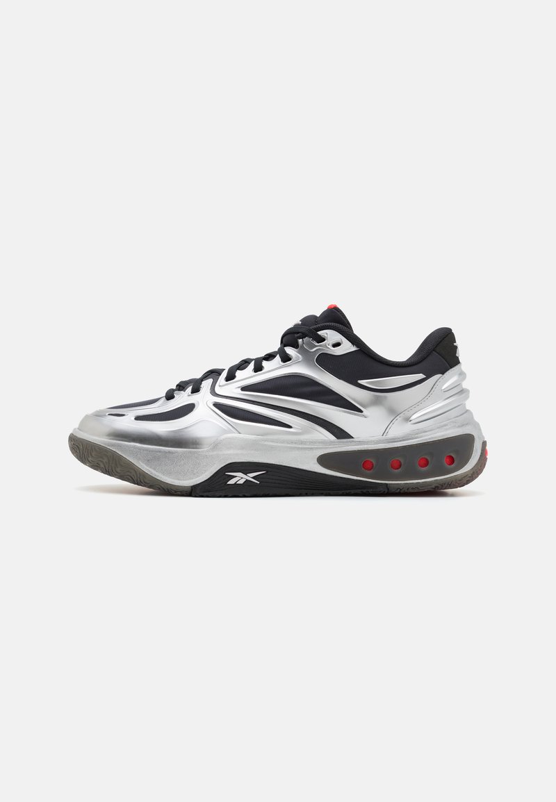 Des chaussures de sport argentées avec un design épuré, une tige en textile noir et des accents rouges. Semelle extérieure en caoutchouc texturé avec des éléments de coussinage visibles.