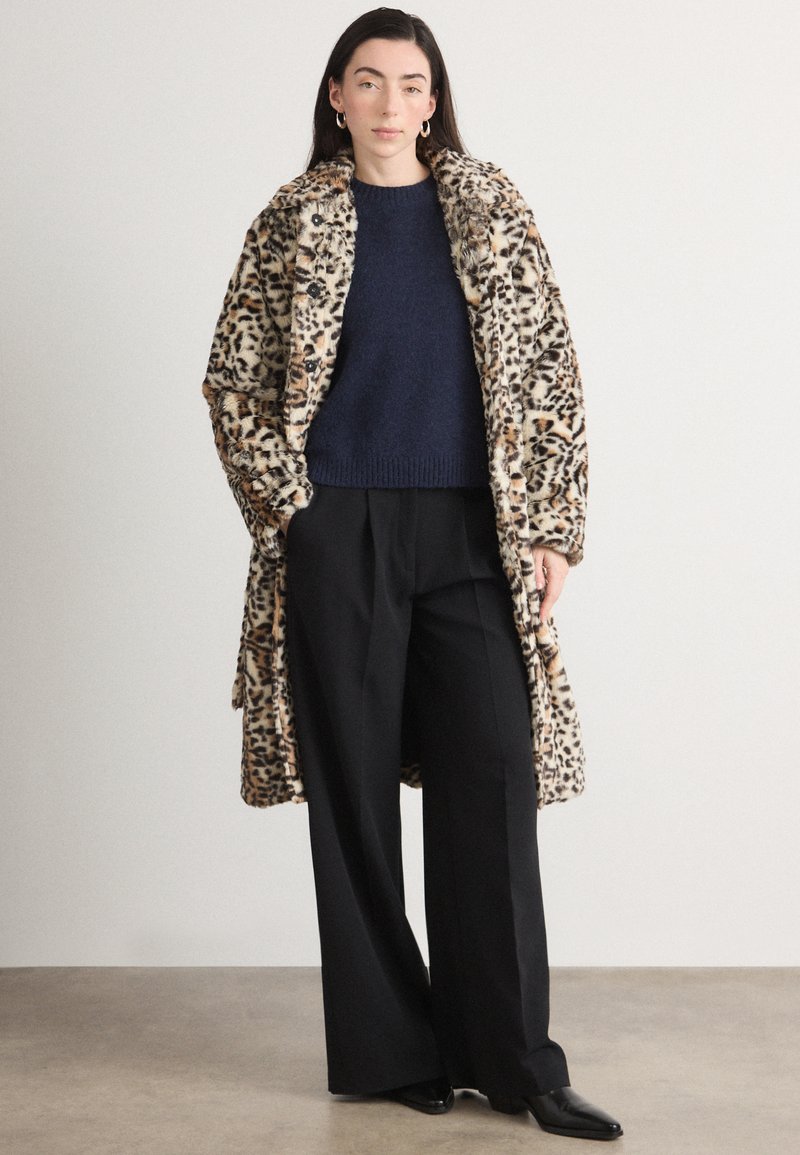 Oversized faux fur frakke med leopardmønster, navy striktrøje, sorte brede bukser, glat tekstur, knapdetaljer og en afslappet pasform.