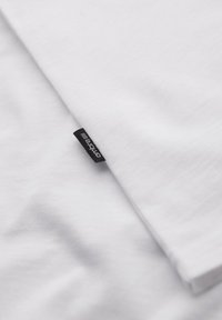 Camiseta de algodón blanca con una textura suave, que presenta una etiqueta de marca negra en el dobladillo, doblada para mostrar su diseño limpio.