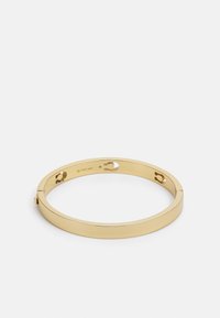 Gold-tone metal bangle bracelet with a smooth, rounded design, featuring a clasp and small circular cutouts for added detail.