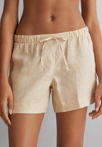 Pantalones cortos de lino beige con cintura elástica y cordón. Ofrecen un ajuste cómodo con un dobladillo recto y una textura sutil.