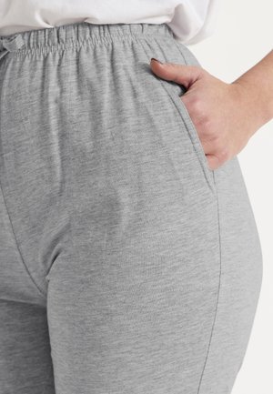 Hånd hvilende inde i lommen på lysegrå joggingbukser med elastik i taljen, båret med en hvid skjorte.