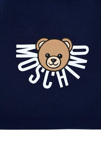 Tessuto blu navy con un volto di orso cartoon in marrone, con occhi neri e un sorriso. Il testo "MOSCHINO" è in lettere bianche in grassetto intorno.