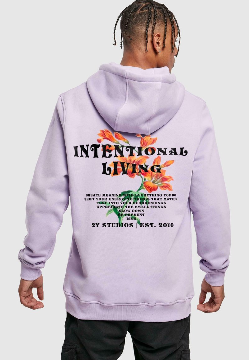 Felpa di colore lavanda con una grande grafica sulla schiena, che presenta accenti floreali e testo audace che recita "VITA INTENZIONALE" e frasi aggiuntive.