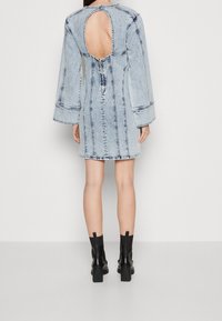 Džínové šaty s dlouhými rukávy, světle modré barvy, detail výřezu na zádech, vertikální šití a zapínání na zip. Nosené s černými kotníkovými botami.