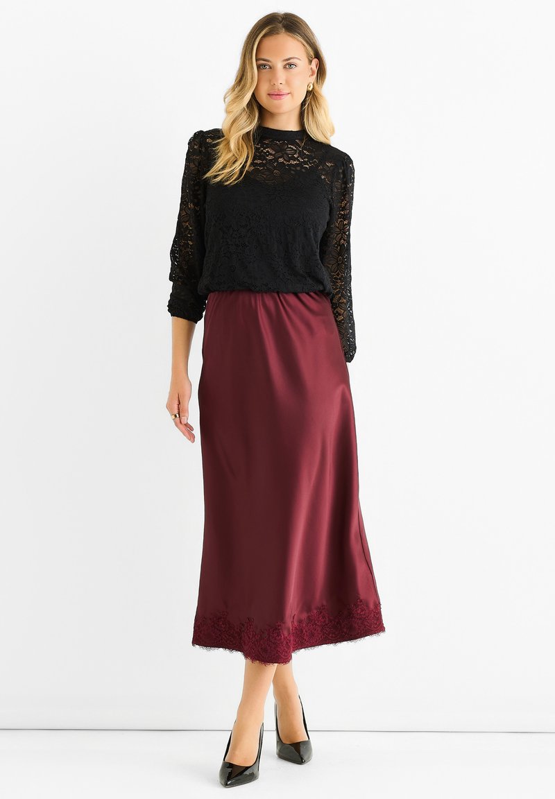 Lace black top with long sleeves paired with a burgundy satin skirt, featuring lace trim at the hem and black high-heeled shoes.