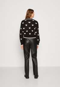 Črna pletena jopica z belimi motivi srca, z rebrastimi manšetami in robom, v kombinaciji z visokim črnim usnjenim hlačami, obuta v črne gležnjarje.