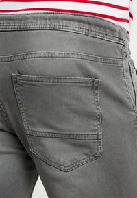 Pantalones de mezclilla gris que cuentan con un bolsillo trasero con un contorno cosido, mostrando una textura ligeramente deslavada y detalles de costura en contraste.