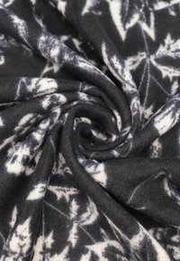 Tessuto a motivi in bianco e nero con una finitura morbida e testurizzata, caratterizzato da foglie a spirale in diverse sfumature di grigio su uno sfondo scuro.