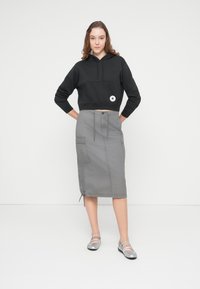 Μαύρη κομμένη φούτερ με μπροστινή τσέπη και λογότυπο, συνδυασμένη με φούστα μεσαίου μήκους σε γκρι χρώμα, με τσέπες cargo και κλείσιμο με κορδόνι. Ασημί μπαλαρίνες.