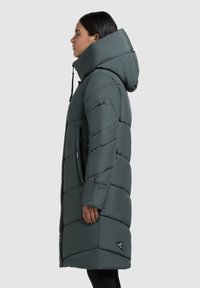 Mid-length, dark green puffer coat with a large hood, featuring a zippered front, side pockets, and diagonal quilted pattern.