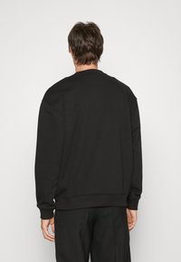 Sudadera negra con cuello redondo, hombros caídos y puños y dobladillo de canalé. Textura de tejido suave con un diseño minimalista.