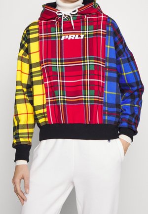 Kapuzenpullover mit rot-, gelb- und blaukarierten Einsätzen, weißen Kordeln, schwarzen Bündchen und Bund, getragen mit weißen Hosen.